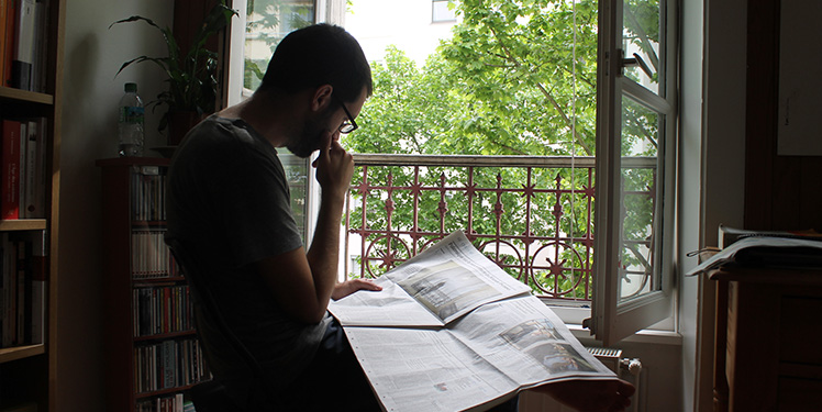 A man reading a newspaper in front of the window